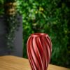 Ira Vase – Dark Red Lifestyle Ira vase in dark red displayed against a green foliage backdrop