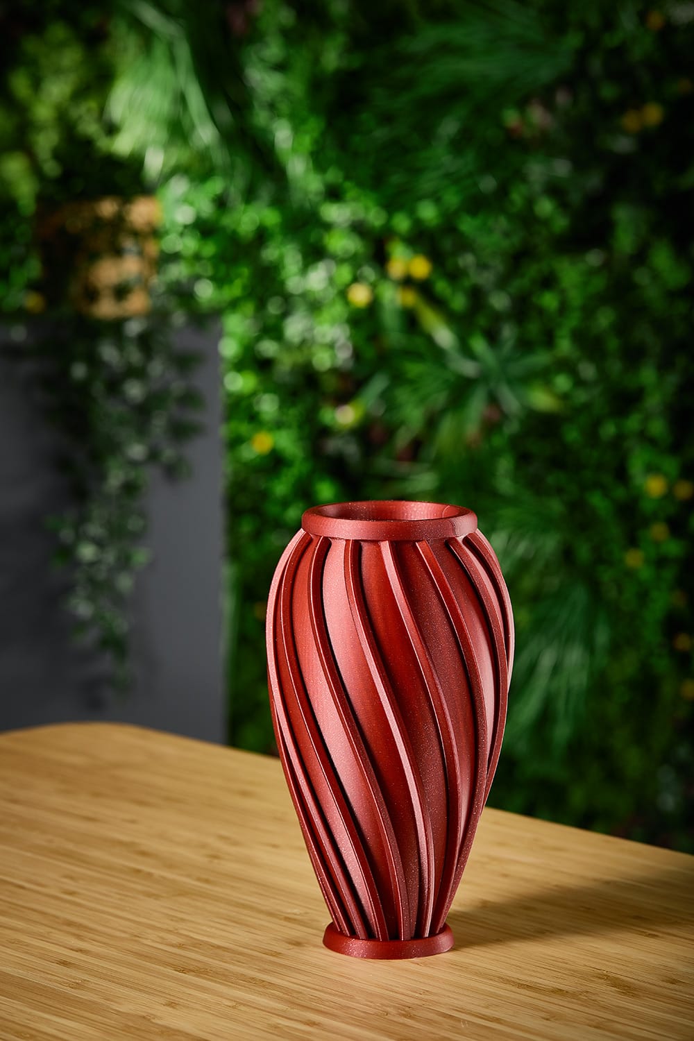 Ira vase in dark red displayed against a green foliage backdrop